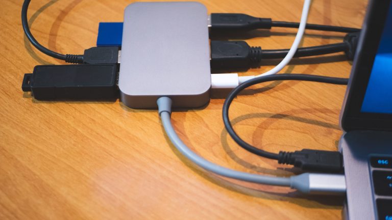 Eine kabelgebundene Dockingstation h&auml;ngt an einem Laptop. In die Dockingstation eingesteckt sind mehrere Kabel und ein USB-Adapter.