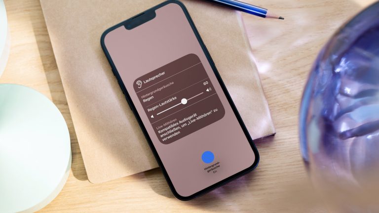 Ein iPhone liegt auf einem Notizbuch zwischen Deko-Elementen. Auf dem Bildschirm ist die Detailansicht für die Hintergrundgeräusche im Kontrollzentrum geöffnet.