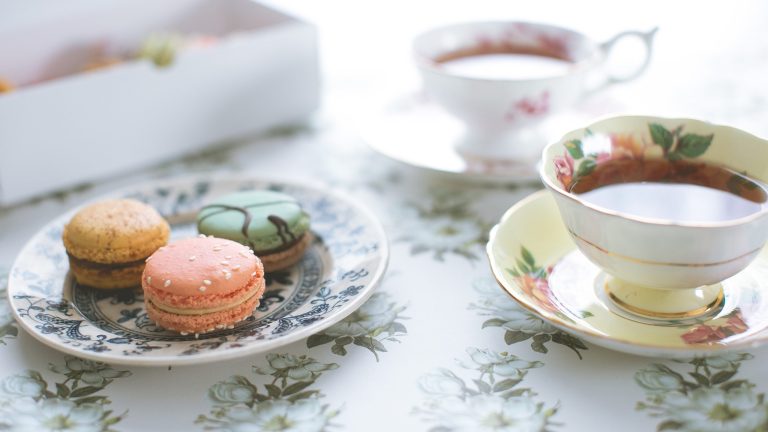 Auf einem Tisch stehen ein Porzellanteller mit drei Macarons und zwei Tassen mit Tee.