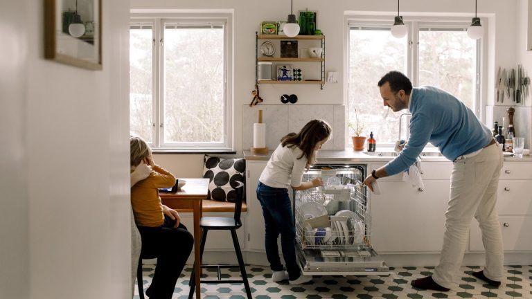 Eine Person räumt gemeinsam mit einem Kind eine Spülmaschine ein.