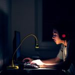 Eine junge Person sitzt in der Dunkelheit vor einem Rechner.