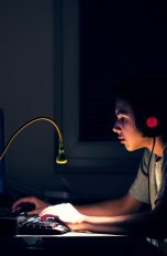 Eine junge Person sitzt in der Dunkelheit vor einem Rechner.