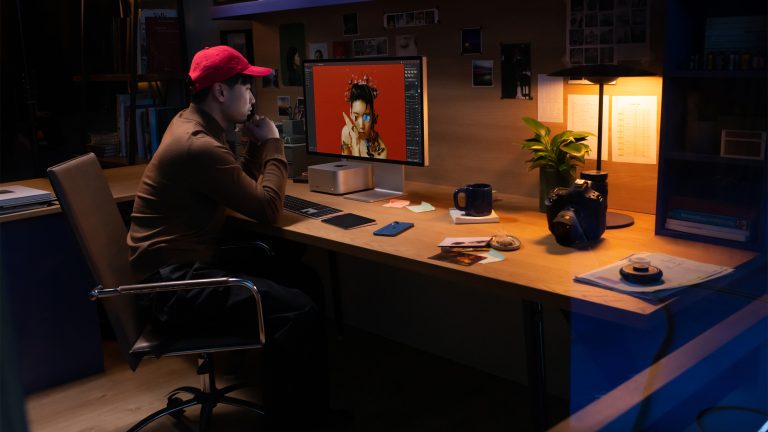 Eine Person sitzt an einem Schreibtisch, auf dem ein Apple Studio Display steht.