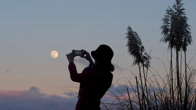 Eine Person fotografiert während des Sonnenuntergangs den Mond mit einem Smartphone.