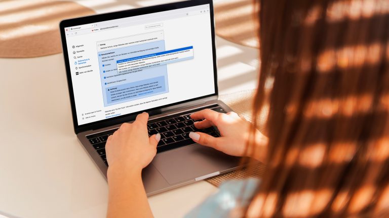 Eine Person sitzt vor einem MacBook und stellt Feinheiten bei der Cookie-Blockade von Firefox ein.