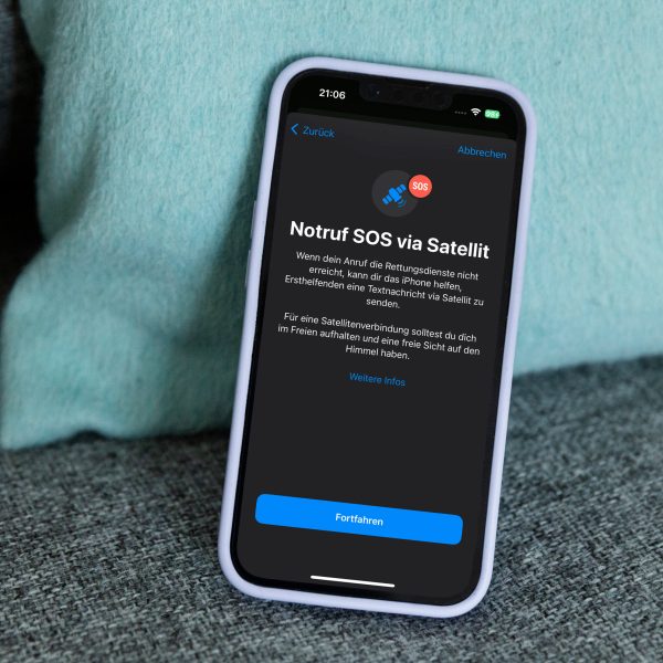 Ein iPhone 14 lehnt auf einem Sofa an einem Kissen. Auf dem Bildschirm ist der Startscreen zum Notruf SOS &uuml;ber Satellit zu sehen.