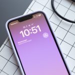 Ein iPhone 13 liegt auf einer Schneidematte. Auf dem Display werden der Sperrbildschirm und einige Symbole in der Statusleiste angezeigt.