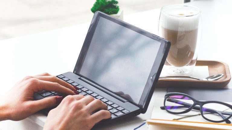 Eine Person sitzt vor einem Netbook und tippt auf dessen Tastatur.