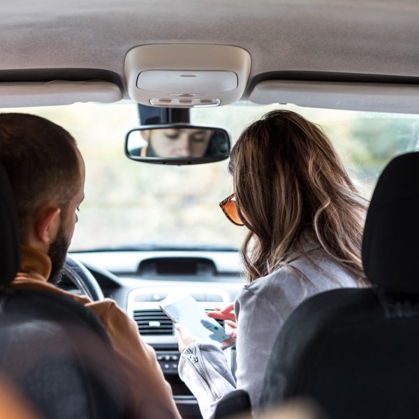 Zwei Personen sitzen in einem Auto. Die eine schaut auf ihr Smartphone.