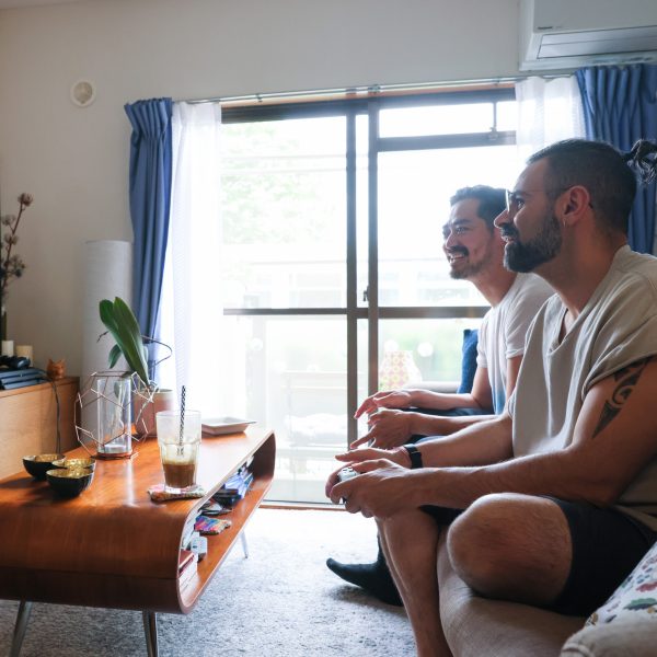 Zwei Personen sitzen auf einem Sofa vor dem Fernseher und halten Controller einer Spielekonsole in der Hand.