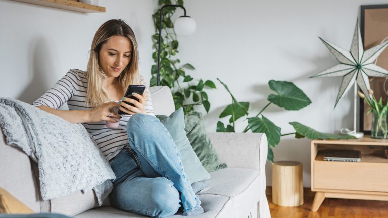 Eine Person sitzt auf einem Sofa und schaut auf ihr Smartphone.