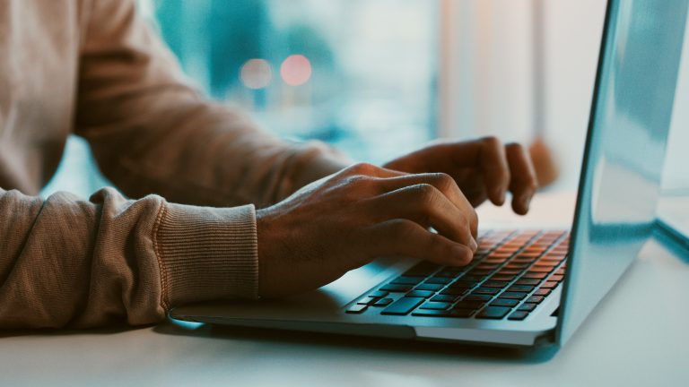Eine Person sitzt vor einem Laptop und tippt auf der Tastatur.