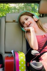 Zwei Kinder mit Kopfhörern auf den Ohren sitzen auf der Rückbank eines Autos.