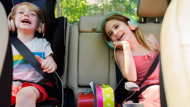Zwei Kinder mit Kopfhörern auf den Ohren sitzen auf der Rückbank eines Autos.