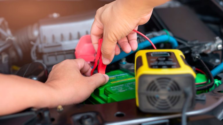 Eine Person steckt ein Batterieladeger&auml;t an eine Autobatterie an.