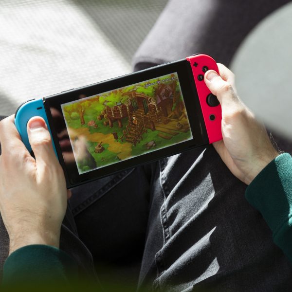 Eine Person sitzt auf einem Sofa und spielt auf der Nintendo Switch im Handheld-Modus.