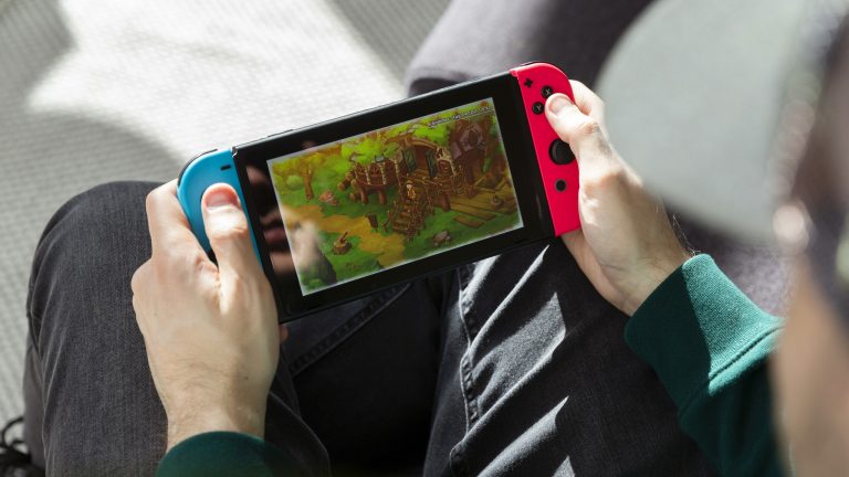 Eine Person sitzt auf einem Sofa und spielt auf der Nintendo Switch im Handheld-Modus.