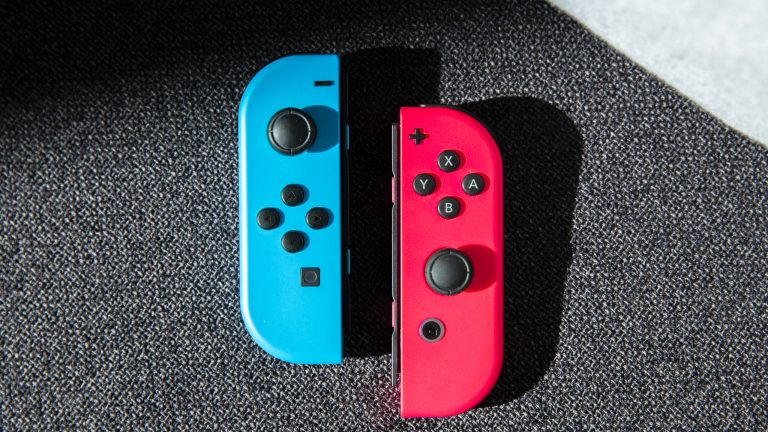 Ein blauer und ein roter Joy-Con liegen nebeneinander auf einem Sofa.
