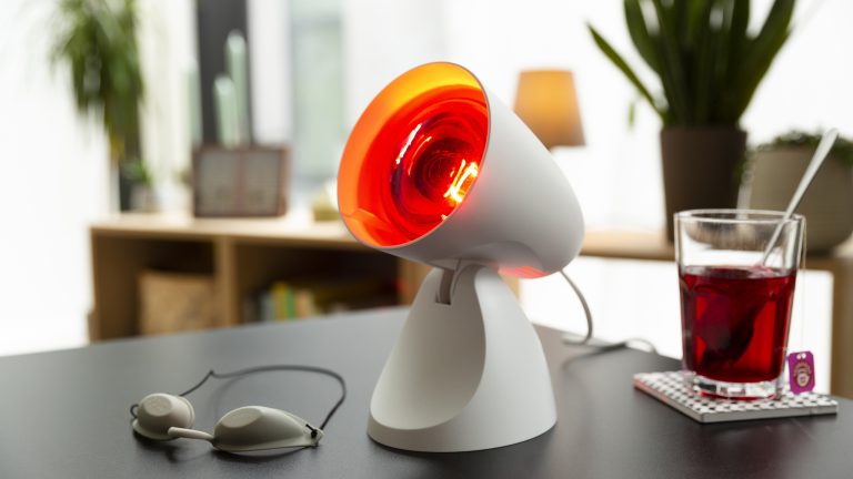 Eine eingeschaltete Rotlichtlampe steht auf einem Tisch. Daneben liegt eine Schutzbrille.