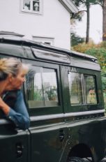 Eine Person fährt einen Geländewagen mit Anhänger rückwärts in eine Auffahrt, eine weitere Person gibt draußen Anweisungen.