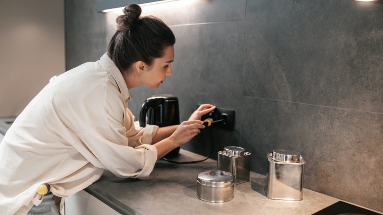 Eine Person schraubt mit einem Schraubendreher eine Steckdosenabdeckung in der Küche ab.