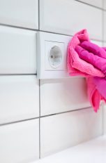 Eine Person mit pinkem Handschuh wischt mit einem pinken Tuch über eine Steckdose.