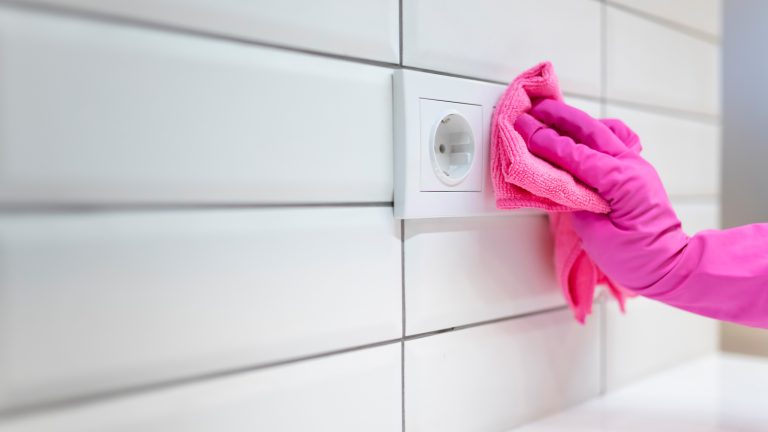 Eine Person mit pinkem Handschuh wischt mit einem pinken Tuch über eine Steckdose.