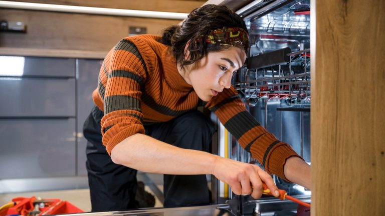 Eine Person kniet vor einem Geschirrspüler und repariert ihn.