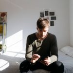 Eine Person sitzt auf einem Bett und bedient ihr Smartphone.