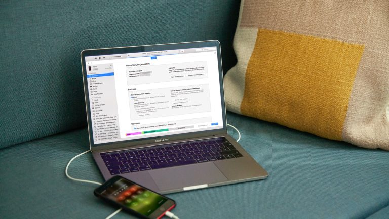 Ein iPhone ist an ein MacBook angeschlossen, auf dem iTunes geöffnet ist.