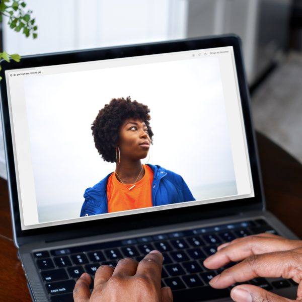 Auf einem Laptop ist das Bild einer Person zu sehen. Der Hintergrund ist Schwarz-Grau.