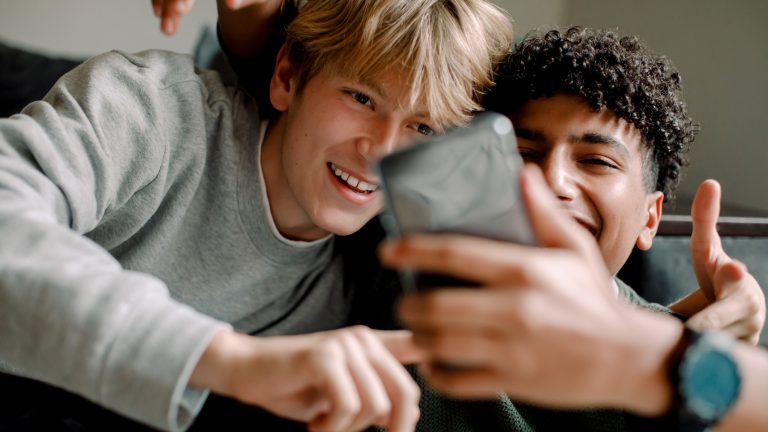 Zwei Personen liegen entspannt auf einem Sofa und albern vor einem Smartphone herum, das eine Person in der Hand h&auml;lt.