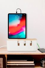 Ein iPad steht auf einer Kabelbox, die wiederum auf einem Schreibtisch aus hellem Holz gestellt wurde.