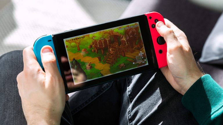 Eine Person h&auml;lt eine Nintendo Switch in der Hand und spielt ein Spiel darauf.
