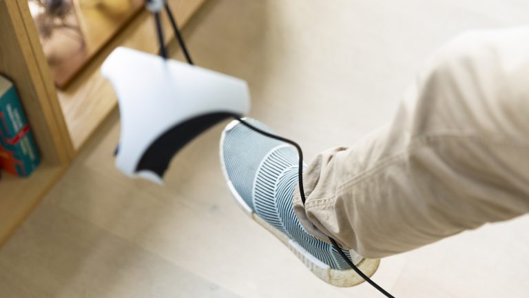 Um einen Fuß ist das Kabel der PSVR 2 gewickelt. Im Vordergrund hängt unscharf ein Sense-Controller ins Bild.