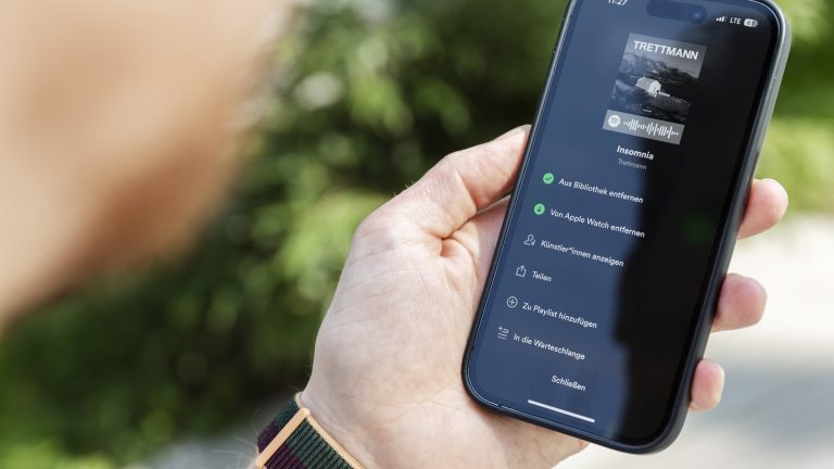 Nahaufnahme eines iPhone 14 Pro, das gerade anzeigt, dass ein Album bei Spotify auf eine Apple Watch heruntergeladen worden ist.