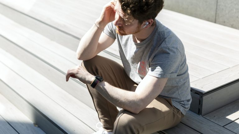 Eine Person sitzt auf einer Treppe und schaut auf ihre Apple Watch. In den Ohren trägt sie Apple AirPods Pro.