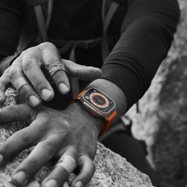 Eine Person beim Klettern trägt eine Apple Watch Ultra, die das exklusive Wegweiser-Zifferblatt trägt. Das Foto ist bis auf die Uhr in Schwarzweiß gehalten.
