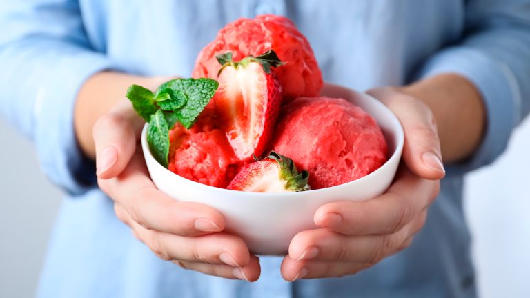 Eine Person hält eine Schüssel mit mehreren Kugeln Erdbeer-Sorbet in der Hand.