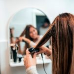 Eine Person steht vor einem Spiegel und glättet sich eine Haarsträhne.