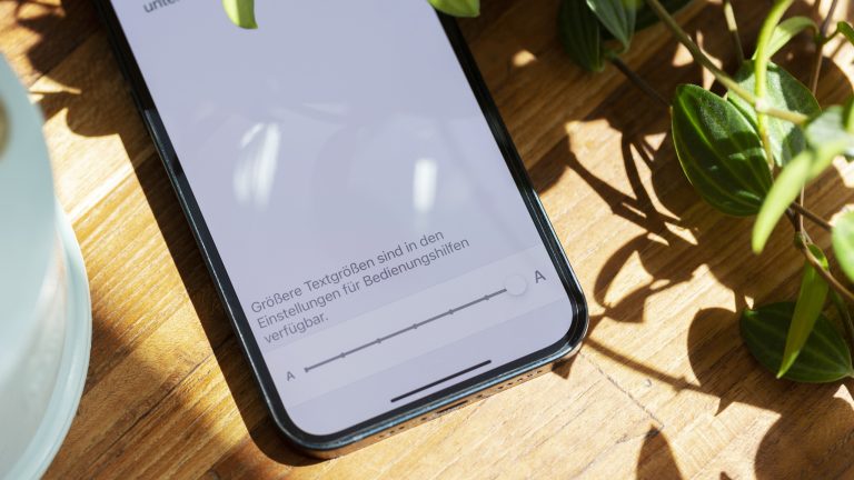 Ein iPhone liegt auf einem Holztisch. Zu sehen ist ein Screenshot der Größen-Einstellungen.