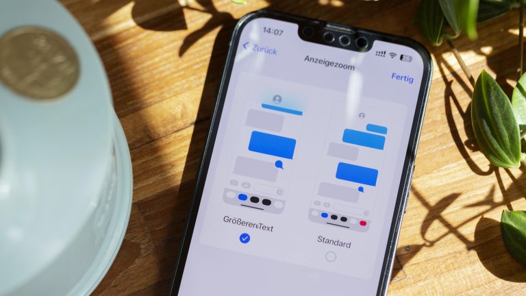 Ein iPhone liegt auf einem Holztisch. Zu sehen ist ein Screenshot der Zoom-Einstellungen.