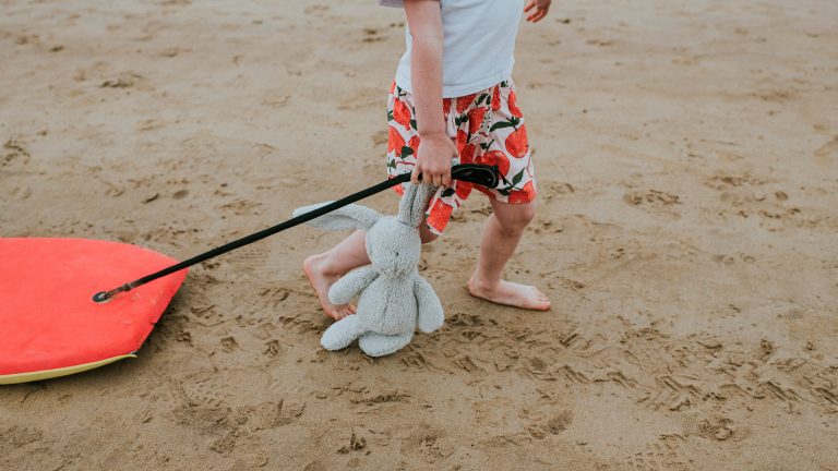 Ein Kind schleift einen Stoffhasen über einen Sandstrand.