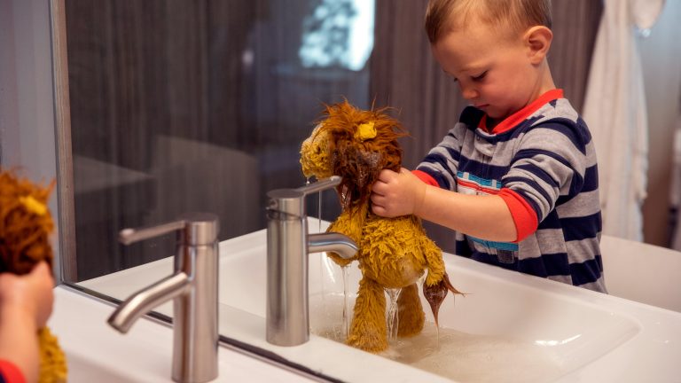 Ein Kind wäscht einen Stoff-Löwen in einem Waschbecken ab.