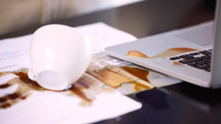 Eine wei&szlig;e Kaffeetasse liegt samt Inhalt ausgebreitet auf Dokumenten und einer Laptop-Tastatur.