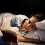 Eine Person liegt im Bett und liest gespannt ein Buch.