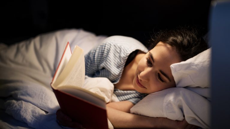 Eine Person liegt im Bett und liest gespannt ein Buch.