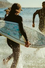 Personen mit Surfbrettern unter dem Arm und Neoprenanzügen laufen ins offene Meer. Personen mit Surfbrettern unter dem Arm und Neoprenanzügen laufen ins offene Meer.