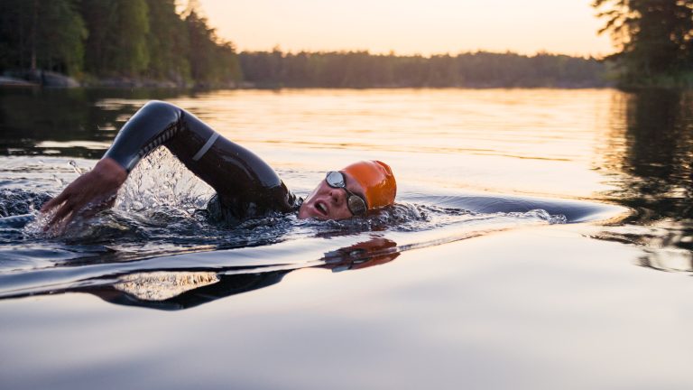 Eine Person in einem Neoprenanzug schwimmt in einem gro&szlig;en See.