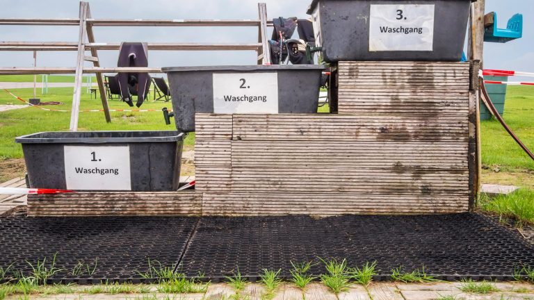 Drei Eimer zum Waschen von Neoprenanz&uuml;gen stehen nebeneinander. Im Hintergrund sind einige Anz&uuml;ge aufgeh&auml;ngt.